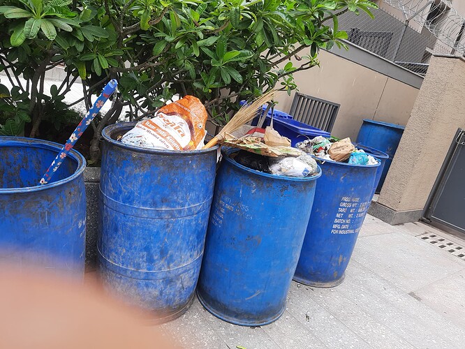 A row of blue garbage bins overflow with trash. (Captioned by AI)