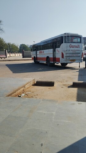 A Guruji bus is parked in a bus station, with some debris scattered on the ground in the foreground. (Captioned by AI)