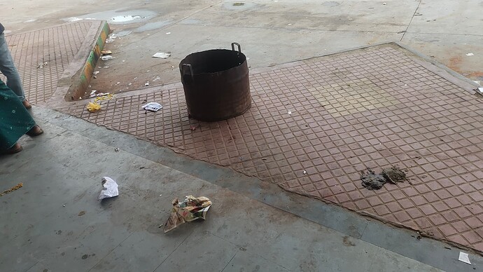 A rusty metal bin sits on a tiled floor littered with trash. (Captioned by AI)