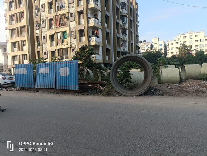 A large concrete pipe sits in front of a building under construction. (Captioned by AI)