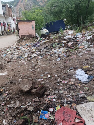 A dirt road is littered with trash in front of a building. (Captioned by AI)