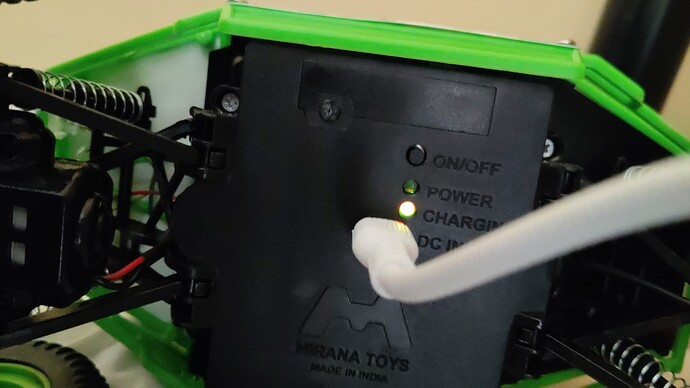 A green toy truck is plugged into a charger, indicating that its battery is currently charging. (Captioned by AI)