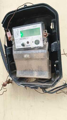 A damaged, dust-covered electricity meter is mounted on a beige wall. (Captioned by AI)