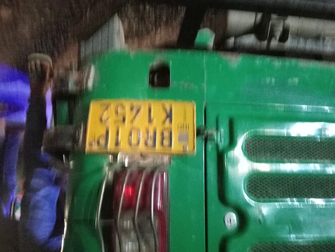 A blurry image of a green vehicle with a yellow license plate that reads "BRO 1P K 1425." (Captioned by AI)